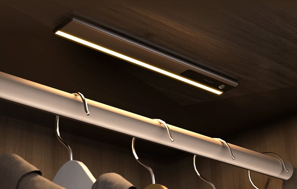 Yeelight light mounted under the shelf in the wooden closet above the rod with hangers.