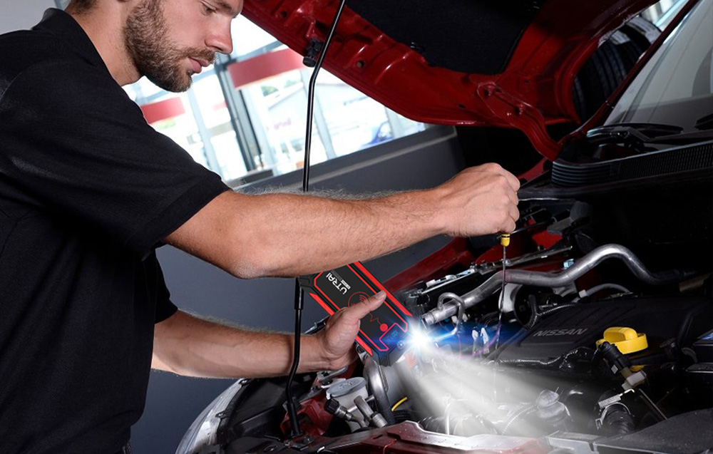 A man illuminates the inside of the car’s hood with a flashlight built into the car starter.