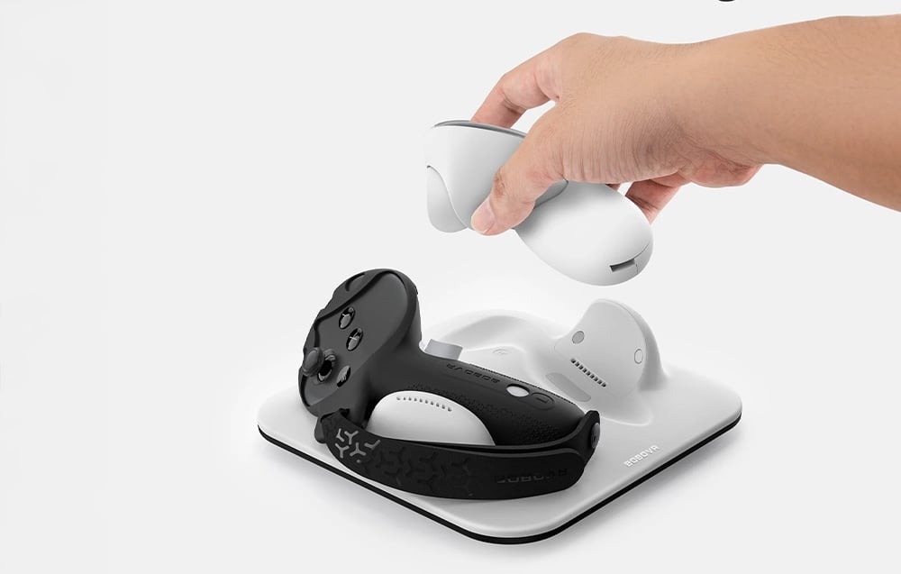 A hand places a VR controller on the white BoboVR CD3 charging station with the second controller already in place