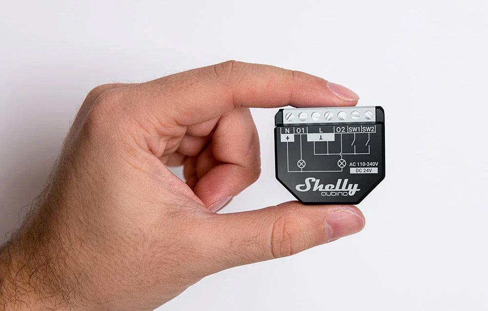 A hand holding a small black light switch with visible electrical connectors and a wiring diagram.
