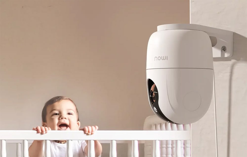 White Imou camera mounted on a wall, with a smiling child in a crib in the background