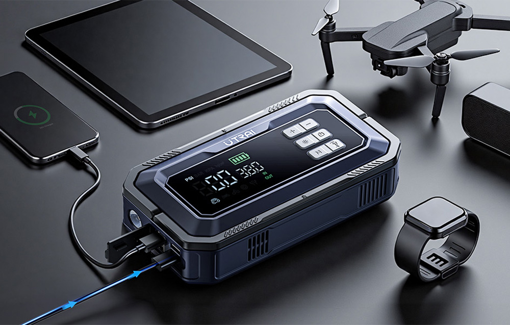 A car starter on a table is charging a smartphone and a tablet next to a watch and a drone.