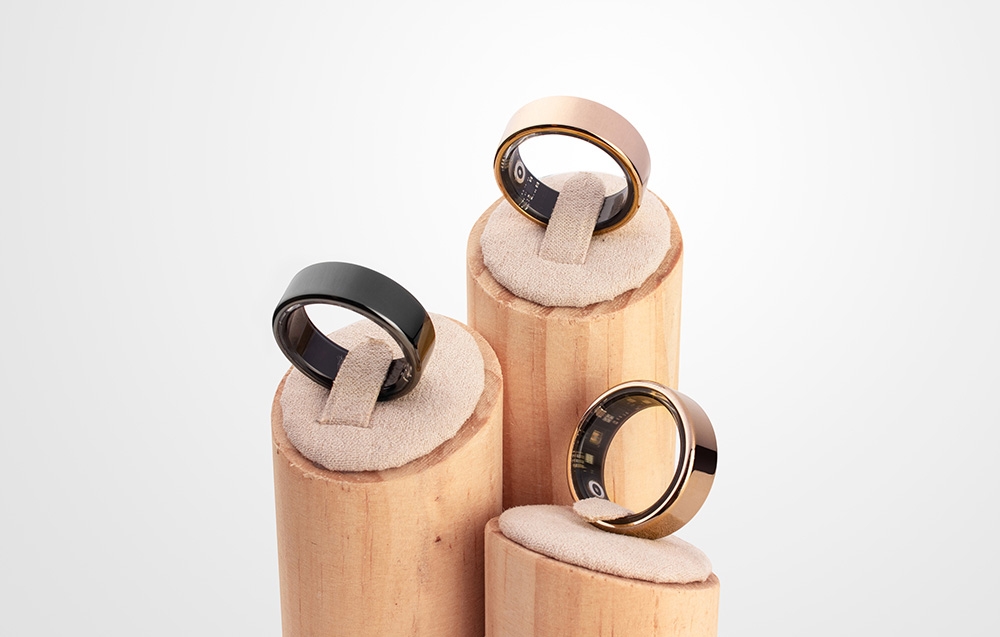 Three smart rings in black and gold on wooden jewelry display stands