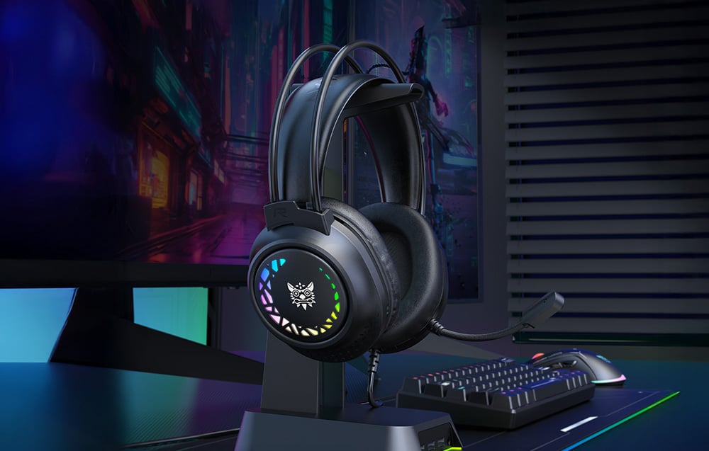 Black gaming headphones on a stand on a desk next to a keyboard, mouse and monitor