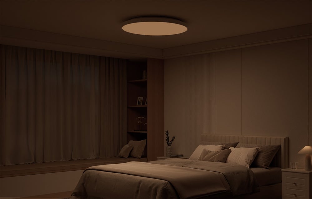 Darkened bedroom interior with bed and Yeelight Mercury C300 smart ceiling lamp shining in warm light.