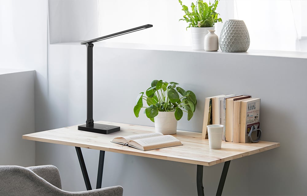 A black lamp on a light-colored table next to a book and a green potted plant
