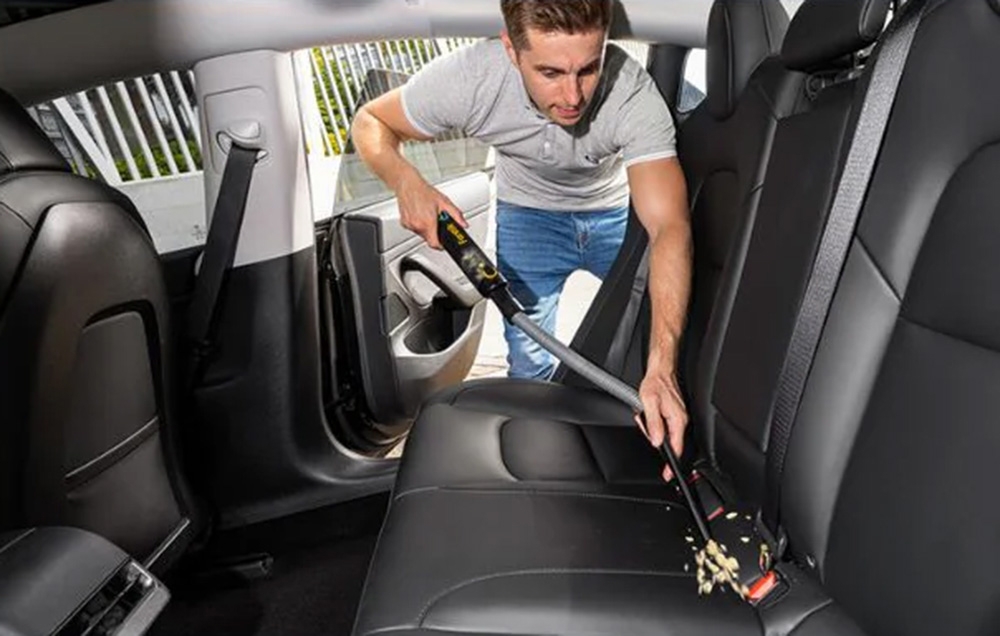 A man removes dirt from a car couch with a portable car vacuum cleaner.
