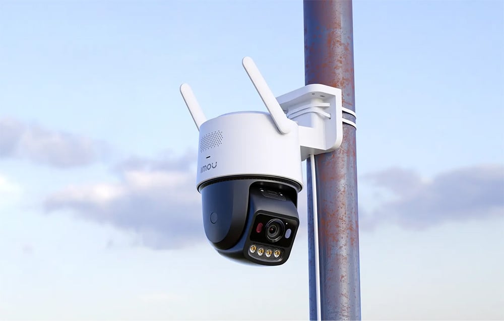 White PTZ camera with two antennas, mounted on a metal pole against a blue sky
