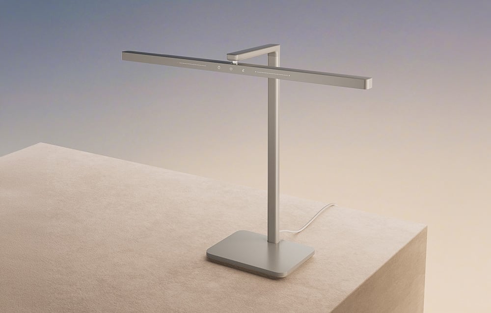 A silver, modern LED desk lamp with a minimalist design, standing on a beige base