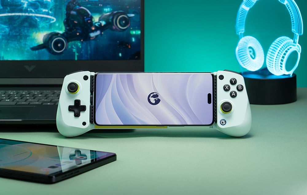 Smartphone mounted in a white GameSir controller set in front of a laptop and headphone-shaped light.
