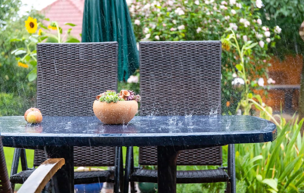 Garden in the rain with water hitting a garden table with a pot and an apple tree