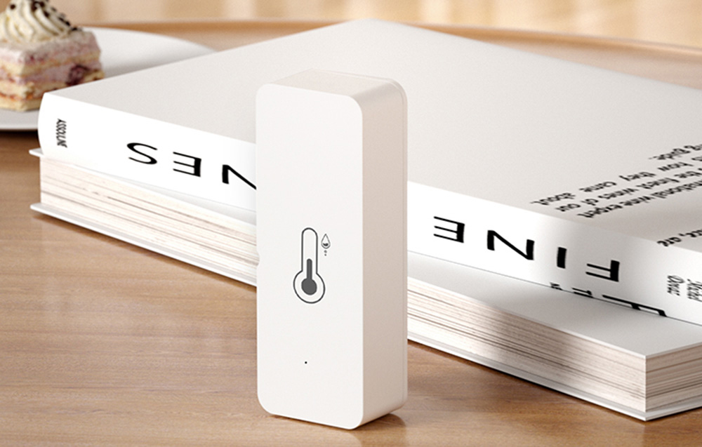 Temperature and humidity sensor set on a table next to a stack of books in a bright room