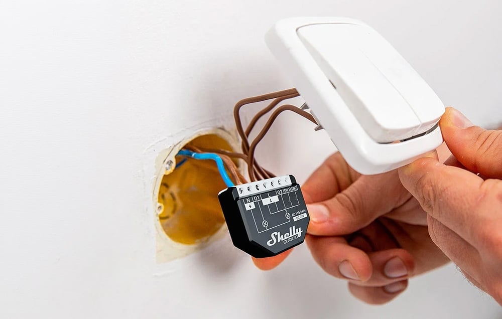A hand is holding the white cover of the switch; the black light switch and wires are visible inside the box.
