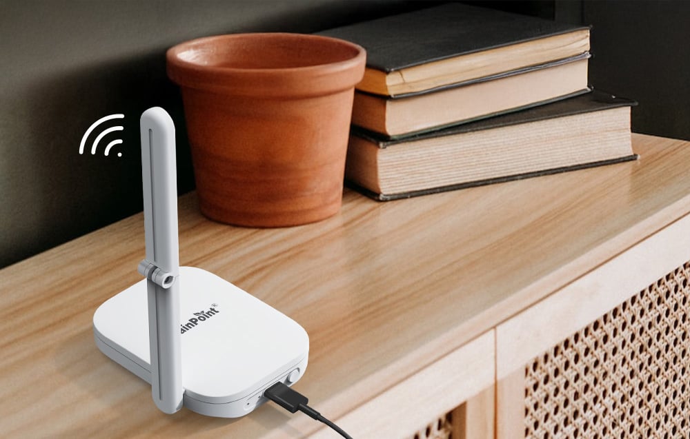 The base station, connected to a USB cable with its antenna raised, sits on a tabletop next to a clay flowerpot and books