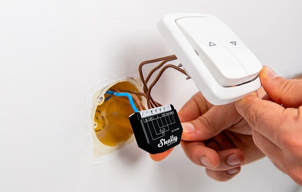 Installation of the controller into an electrical outlet; a hand holds a white switch with two buttons.