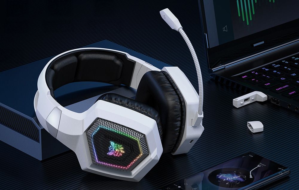 Onikuma gaming headphones lying next to a smartphone and laptop on a black desk