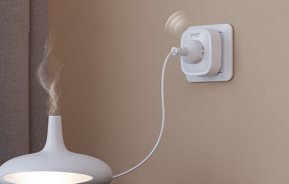A Gosund smart plug with a connected humidifier emitting water vapor, mounted on the wall next to a curtain