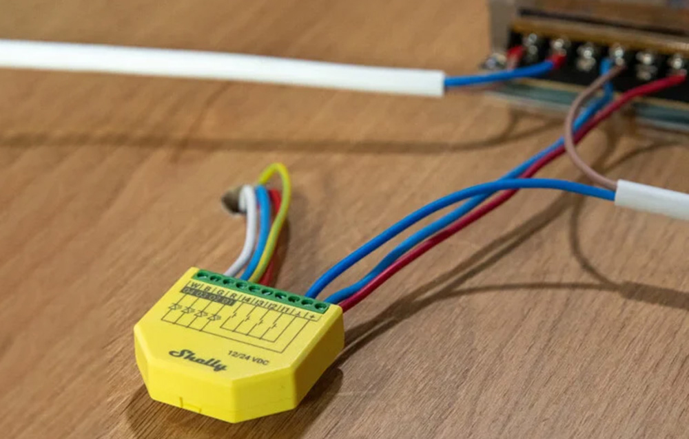 Yellow Shelly LED strip controller with connected wires on a wooden desk