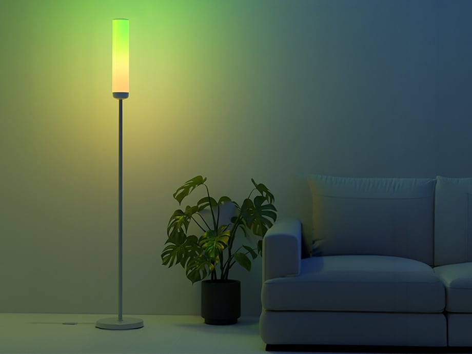 A modern floor lamp emitting yellow-green light, placed in the living room next to a green monstera plant and a light-colored sofa.