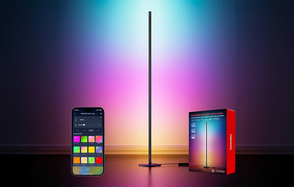 A vertical pillar-shaped floor lamp emitting multicolored light next to a phone and a box.