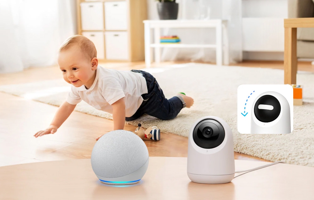 A home security camera on a table next to a speaker; in the background, a toddler crawling; next to it, a thumbnail showing the lens being covered.