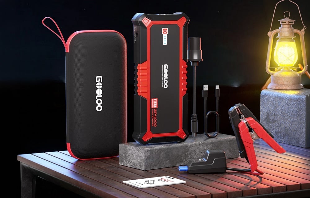 Car starter kit with case, cables, and accessories on a table next to a lamp