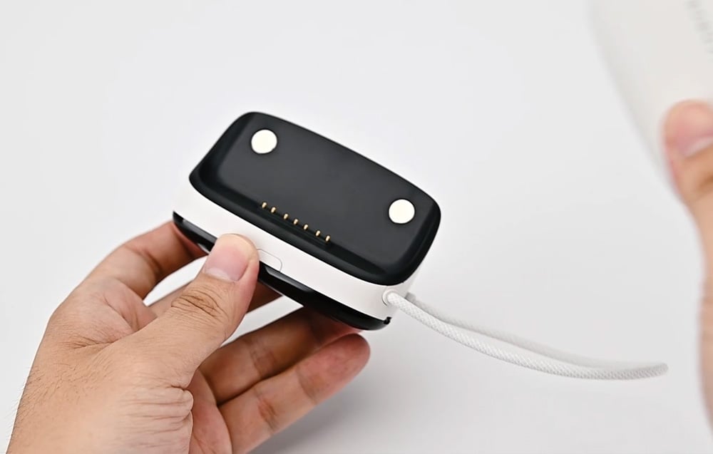 Bottom view of BoboVR PD100 module held in hand, with charging pins and connected cable visible