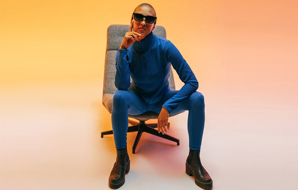 A person in blue sportswear and sunglasses sits on a chair in a colorful studio setting