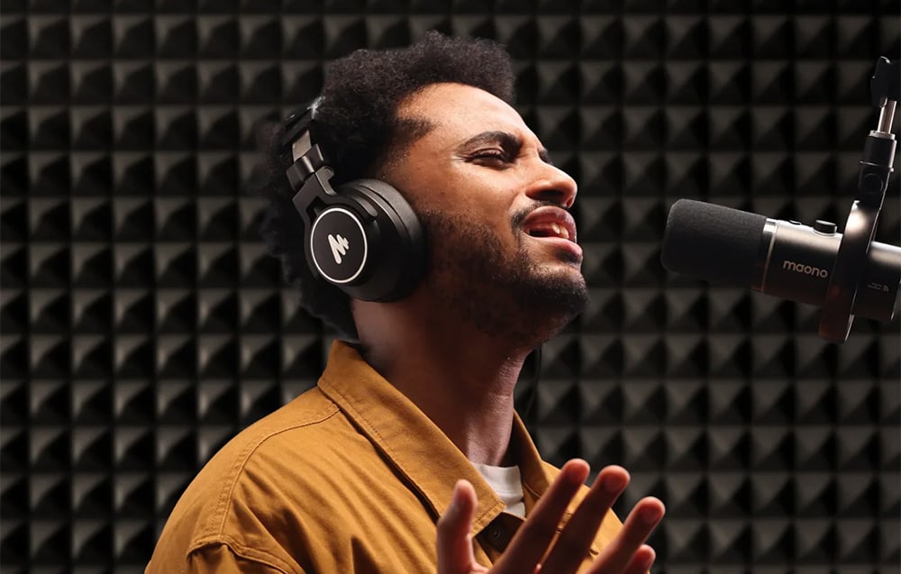 A man wearing headphones singing into a Maono microphone in a soundproof recording studio