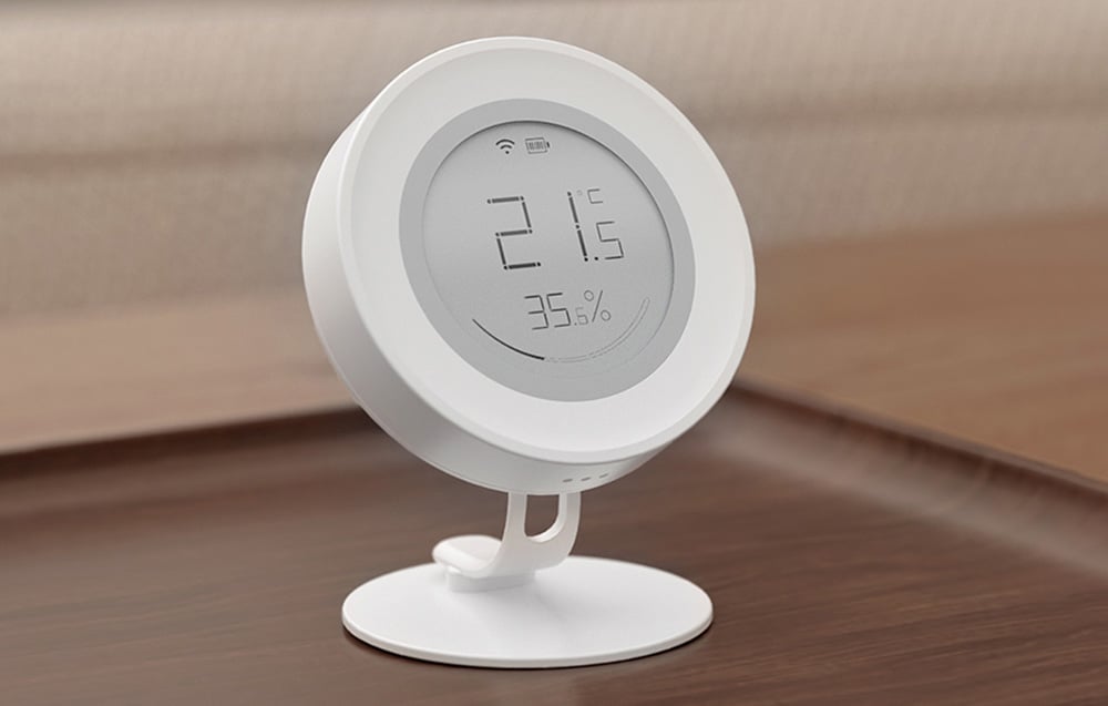 Round white sensor on a stand showing temperature of 21.5°C and humidity of 35.6%, set on a wooden tabletop