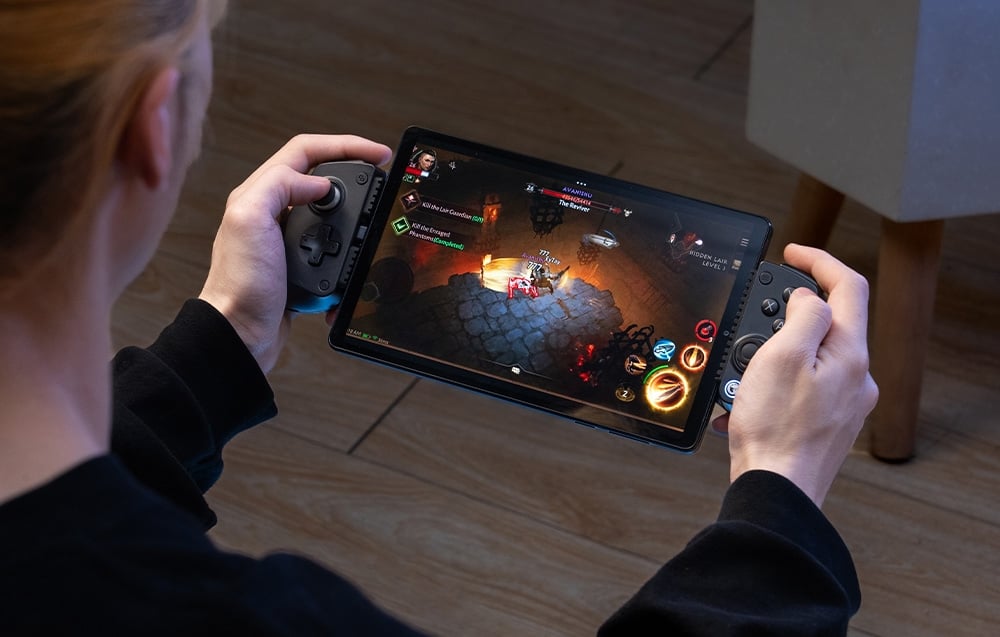 A person holding a tablet with a black GameSir controller at his sides during an RPG game.