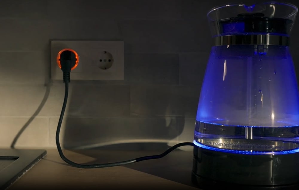 Electric kettle plugged into an outlet with the Shelly Plug S plug glowing red