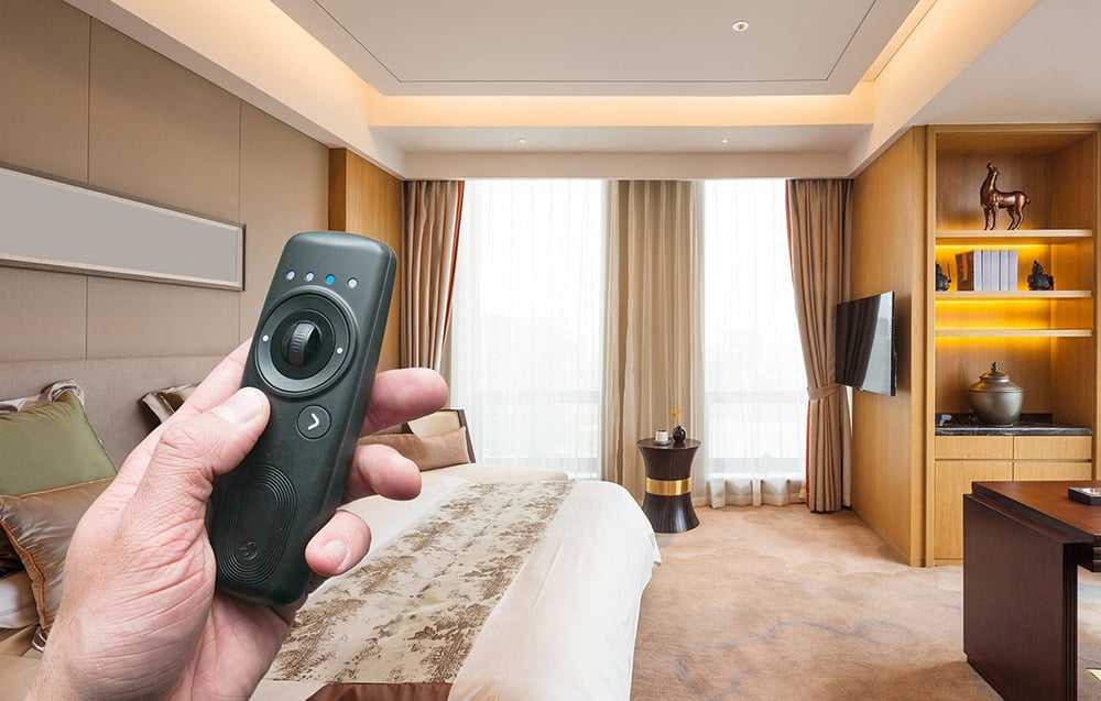 Shelly BLU remote control held in hand, with a bright bedroom with a large window and soft lighting in the background
