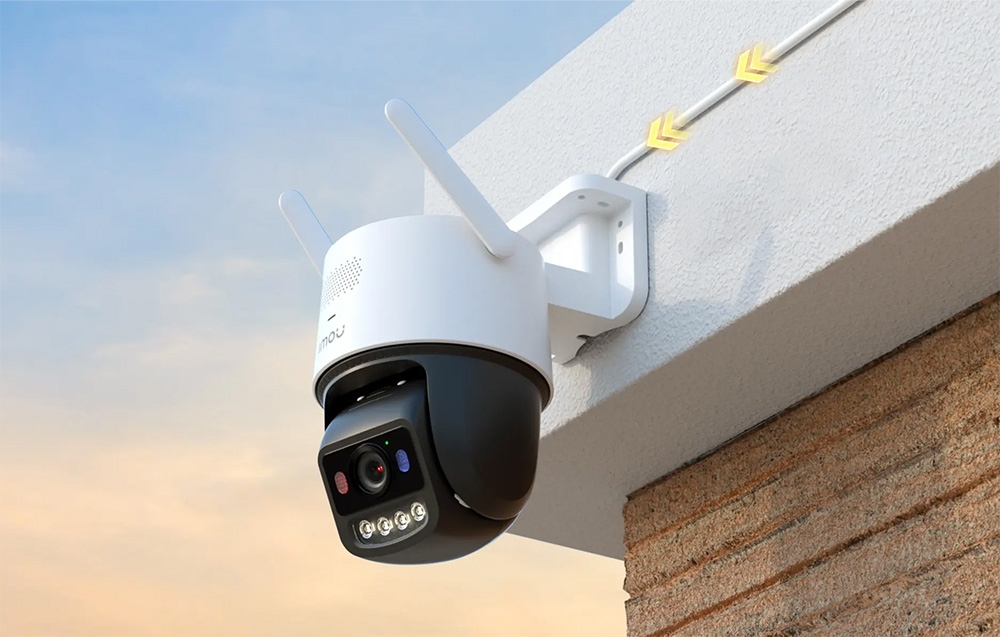 A pan-tilt camera on the corner of the building; yellow arrows symbolizing the flow of electricity are drawn along the power cable