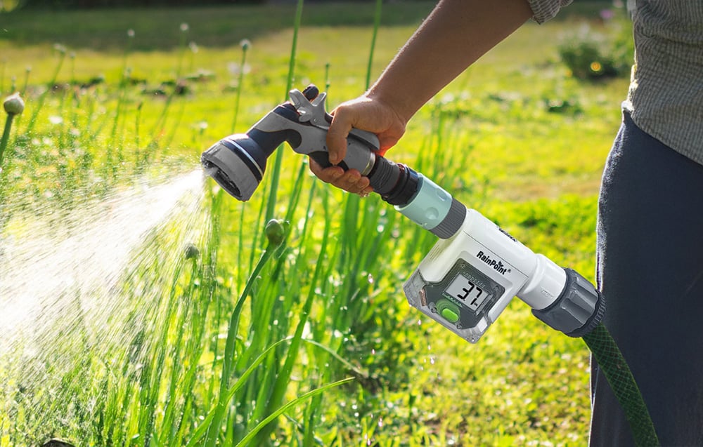 A flow meter mounted between the hose and the spray nozzle while watering garden crops