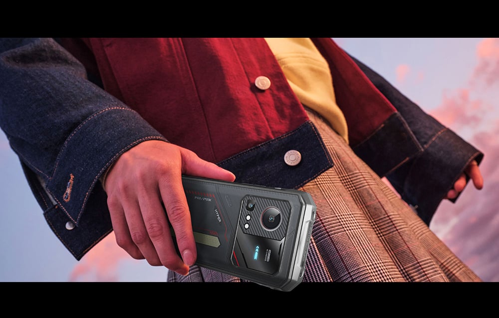 Close-up of a hand holding a HOTWAV smartphone against a backdrop of fashionable styling and a pink sunset sky.