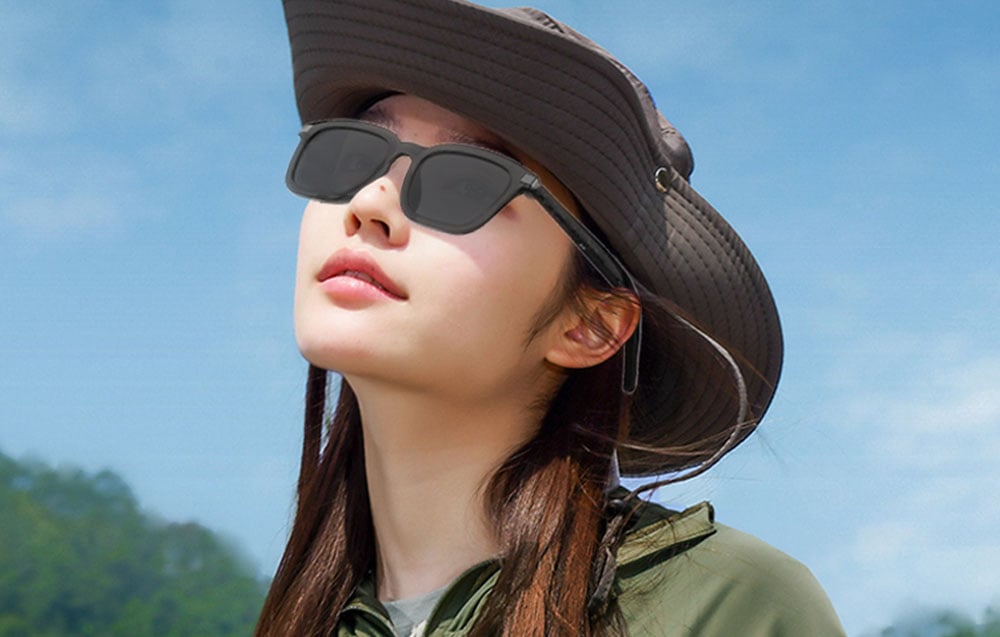 A woman in a travel hat looking up, wearing smart glasses.