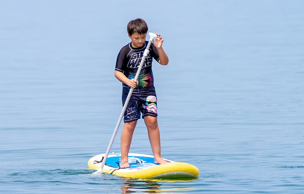 Boy on a surfboard with a paddle in his hand