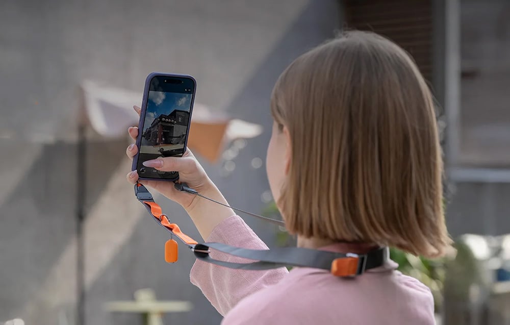 A woman photographing a building with her smartphone mounted to a PGYTECH neck strap