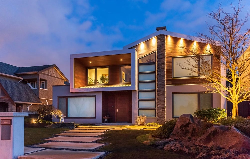 A modern residential building illuminated at dusk, featuring a stone facade and wood trim.