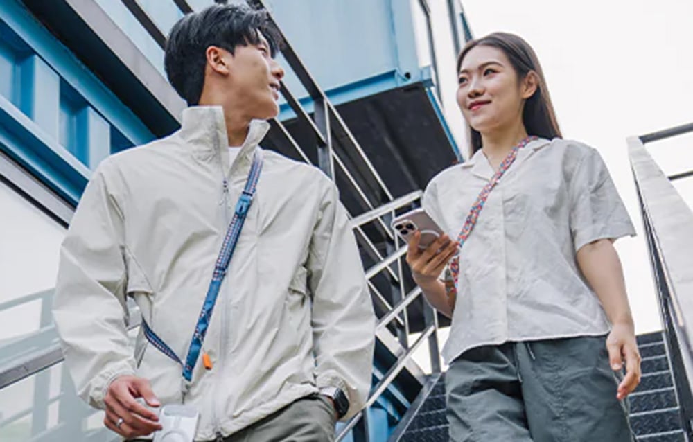 A man and woman walk down the stairs, wearing PGYTECH straps slung over their shoulders