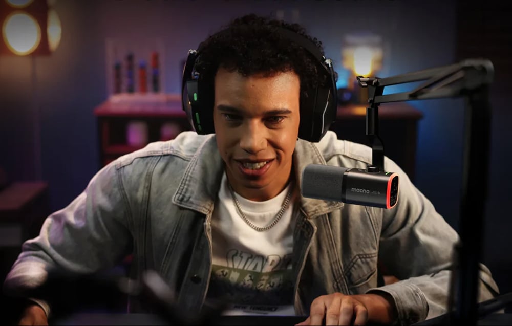 A man wearing headphones looking at a computer screen, with the Maono microphone hanging from an arm in front of him