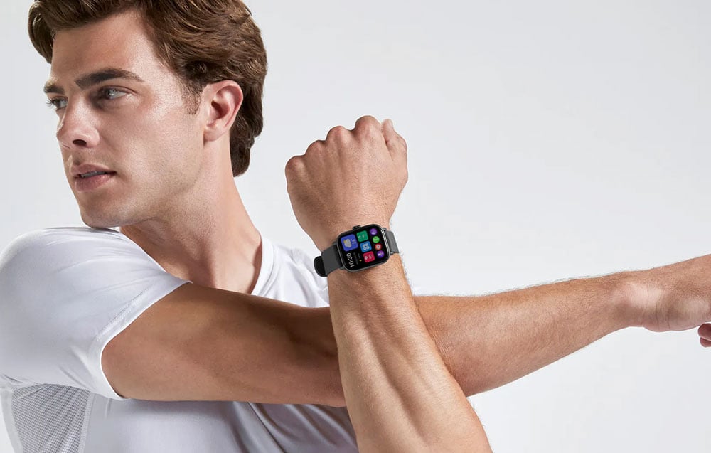 A man in a white sports shirt doing arm stretches, wearing a black smartwatch on his wrist