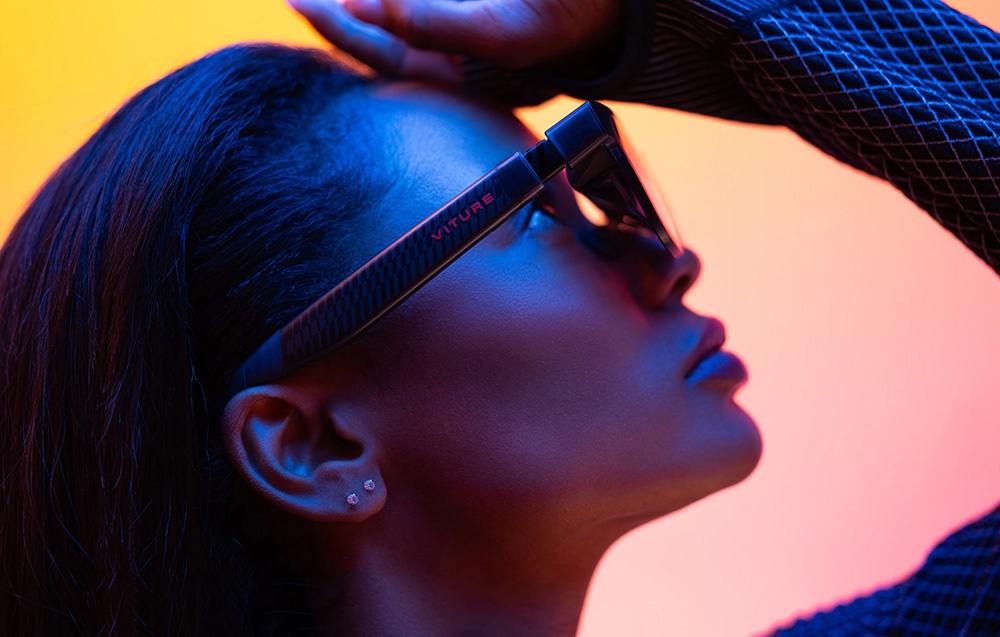 Close-up of a woman wearing Viture brand glasses, with a colorful gradient background and light coming from the side