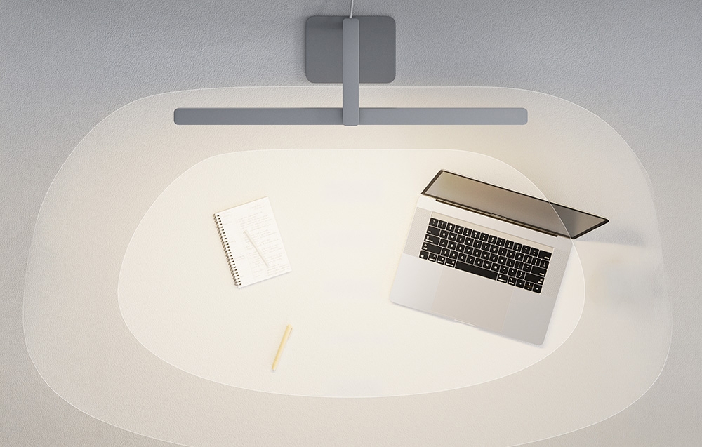 A top-down view of a desk with a laptop and a notebook bathed in the oval, bright beam of a modern lamp