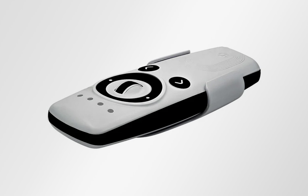 White Shelly remote control with black knobs and buttons, placed in a holder on a light background, seen from a side perspective.