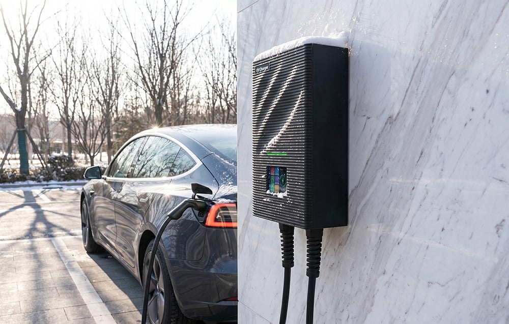 A black car in a parking lot connected to an EV charger with snow visible on it