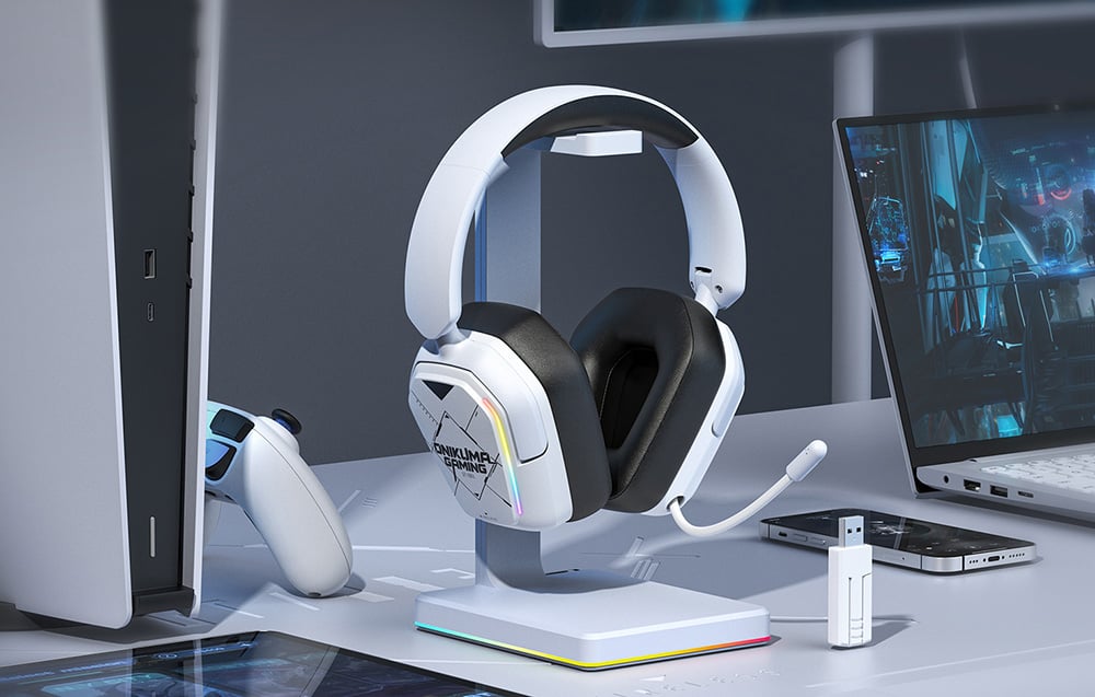 White Onikuma headphones on a stand next to smartphone, console and laptop