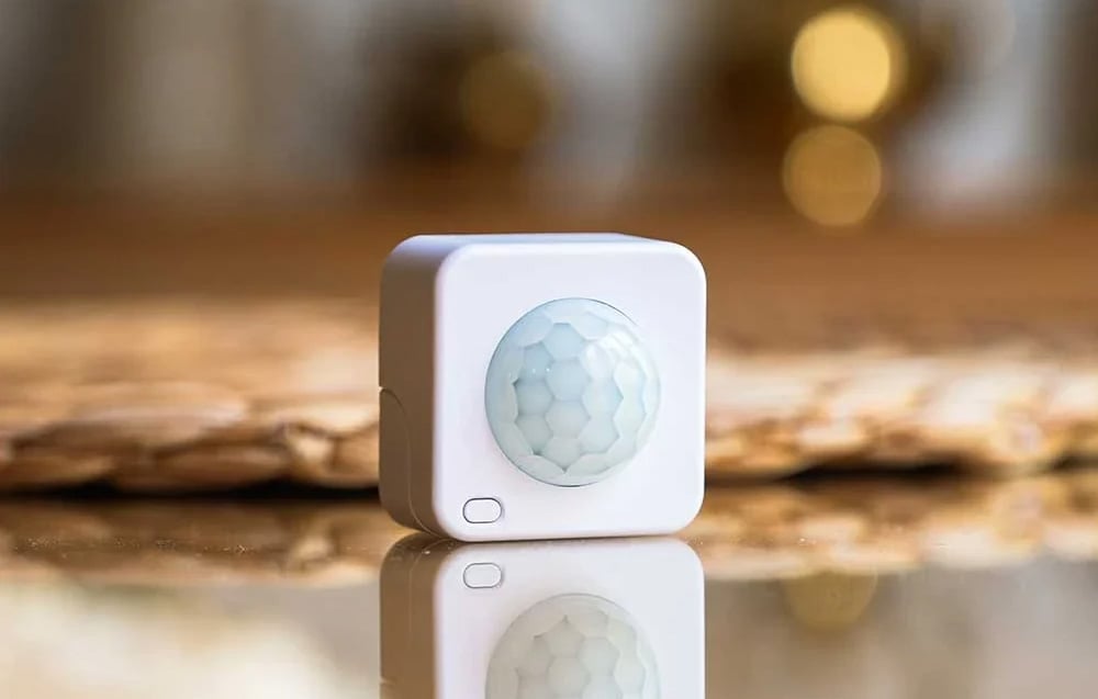 A white, square device with a round, convex lens, standing on a shiny, reflective surface