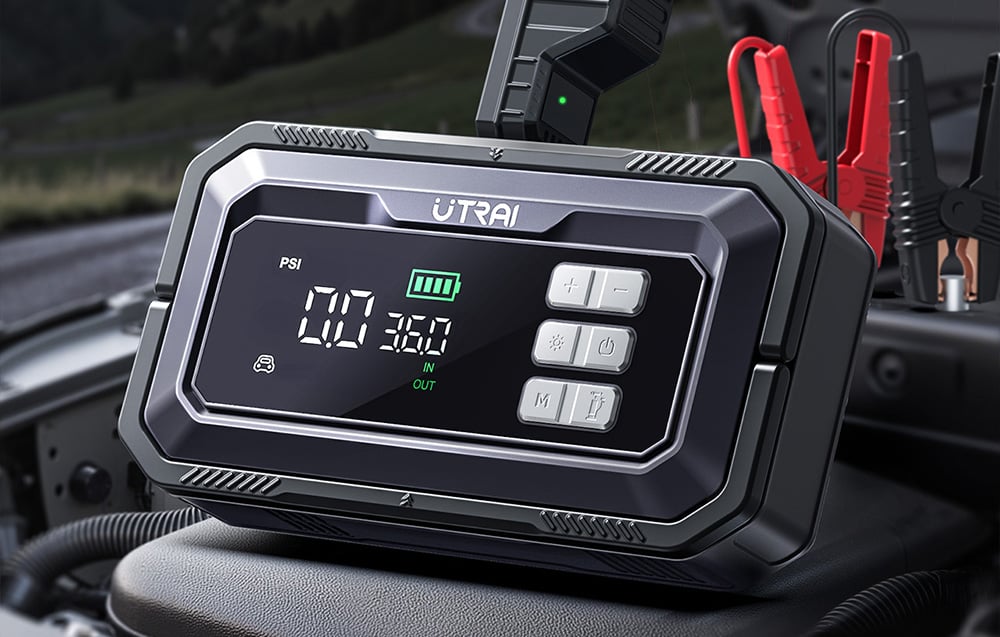 A car jump starter with a digital display lies under the open hood of a car next to the cables.